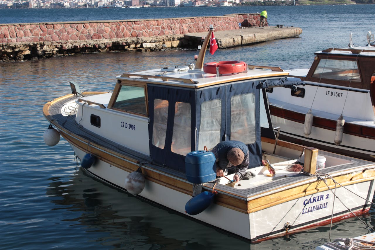 Man repairing moored motorboat with Turkey flag in Çanakkale harbor.
